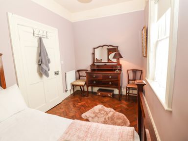 A bedroom with a bed a wooden dresser with a mirror two chairs a lamp and a window at The Merchant's Store in Kilrush Country Clare