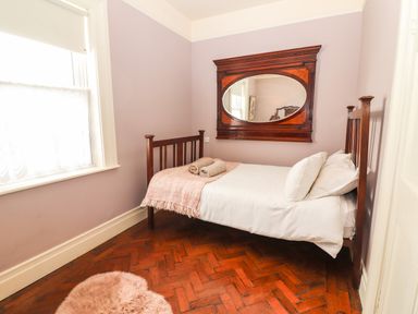 A small bedroom with a single wooden bed white bedding a pink throw two towels a wooden framed mirror on lavender walls and a window with blinds at The Merchant's Store Kilrush Country Clare