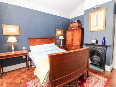A bedroom with a wooden bed a wardrobe two lamps a fireplace and framed pictures at The Merchant's Store in Kilrush Country Clare