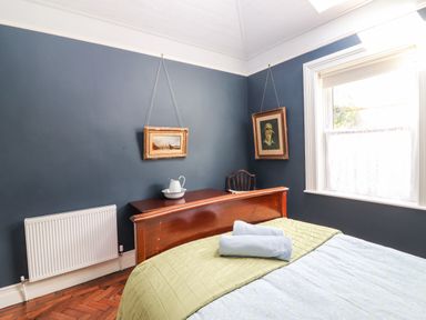 A bedroom with a bed with folded towels a wooden headboard two framed paintings a chair and a window at The Merchant's Store in Kilrush Country Clare