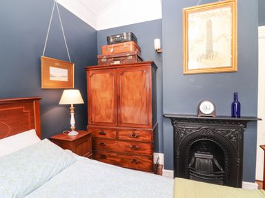 A bedroom with a wooden wardrobe bedside table with lamp bed and an ornate black fireplace at The Merchant's Store in Kilrush Country Clare