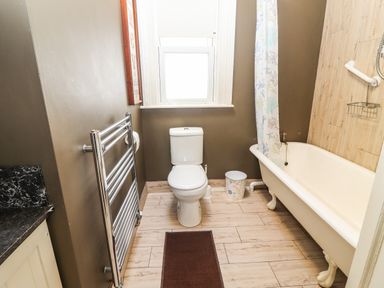 A bathroom with a toilet next to a bathtub with a shower curtain and a stainless steel towel rack at The Merchant's Store in Kilrush Country Clare
