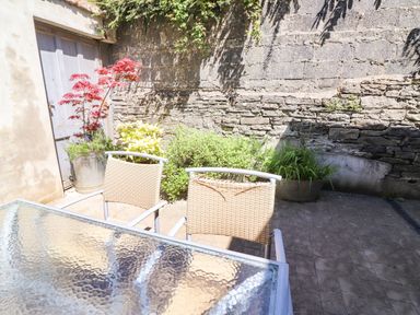 A patio with two chairs and a glass table next to a stone wall with plants at The Merchant's Store in Kilrush Country Clare