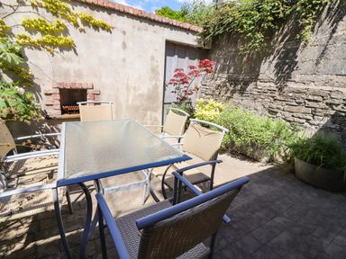 An outdoor patio with a glass table and six wicker chairs surrounded by a brick wall and plants at The Merchant's Store in Kilrush Country Clare