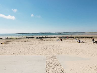 A sandy beach with people walking and sitting near the water at Maelog 14 Tides Reach in Rhosneigr