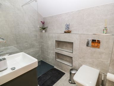 A bathroom with a white sink a toilet a small trash can and decorative items on a tiled wall at Maelog 14 Tides Reach in Rhosneigr