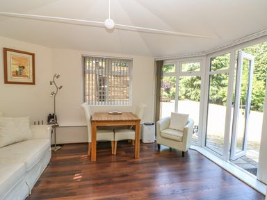 A sitting area with a wooden table and chairs a white armchair and a sofa with large windows and a door leading outside at Badger View in Culverstone Green near Chatham