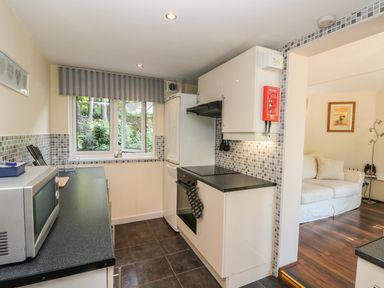 A kitchen with white cabinets black countertops and a microwave next to a living room with a white sofa and wooden floor at Badger View in Culverstone Green near Chatham