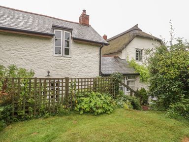 A garden with green plants and a wooden trellis outside white stone cottages at The Old Bakery in Crowcombe