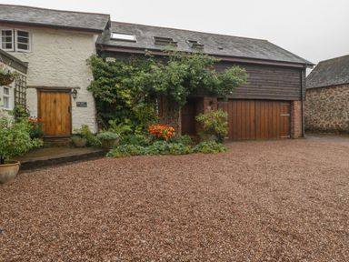 A gravel driveway in front of a house with wooden doors and climbing plants at The Old Bakery in Crowcombe