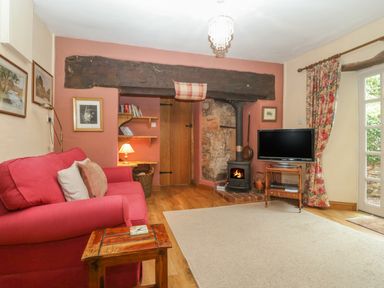A living room with a red sofa a wood stove television and floral curtains at The Old Bakery in Crowcombe
