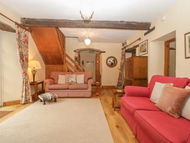 A living room with two sofas a wooden staircase a small footstool and wooden furniture at The Old Bakery in Crowcombe