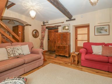 A living room with two sofas a wooden cabinet and a staircase at The Old Bakery in Crowcombe