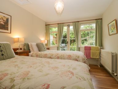 A bedroom with two single beds bedside tables lamps and windows with green curtains at The Old Bakery in Crowcombe