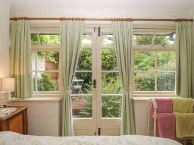 A bedroom with green curtains and a glass door opening to a garden at The Old Bakery in Crowcombe