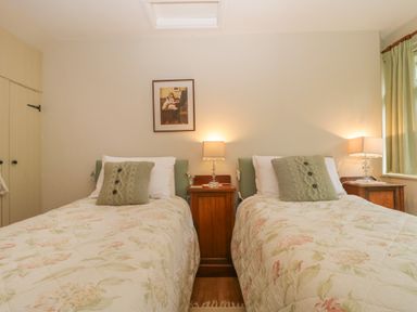 A bedroom with two single beds with floral bedspreads and green cushions two bedside tables with lamps and a framed picture on the wall at The Old Bakery in Crowcombe