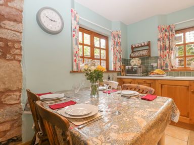 A kitchen with a dining table set for four by windows with floral curtains at The Old Bakery in Crowcombe