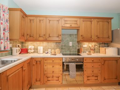 A kitchen with wooden cabinets a gas stove oven sink and various kitchen appliances and utensils at The Old Bakery in Crowcombe