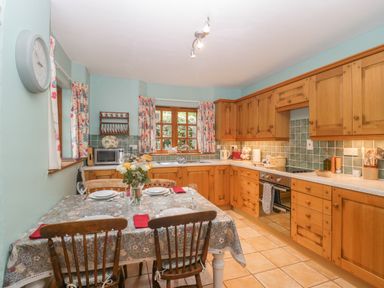 A kitchen with wooden cabinets a dining table set with plates and flowers at The Old Bakery in Crowcombe