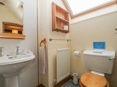 A bathroom with a pedestal sink, a wooden toilet seat, a wall-mounted wooden shelf, a towel ring with a towel, a radiator, and a skylight window at The Old Bakery in Crowcombe