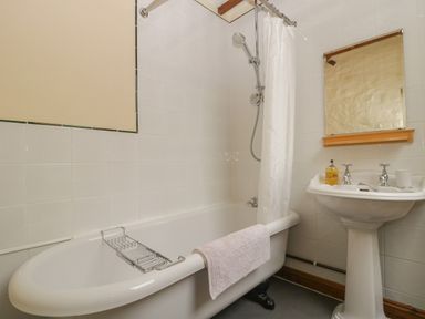 A bathroom with a bathtub shower curtain pedestal sink and mirror at The Old Bakery in Crowcombe
