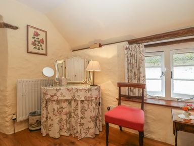 Vanity table with a floral cloth a chair with red upholstery beside a window with curtains at The Old Bakery in Crowcombe