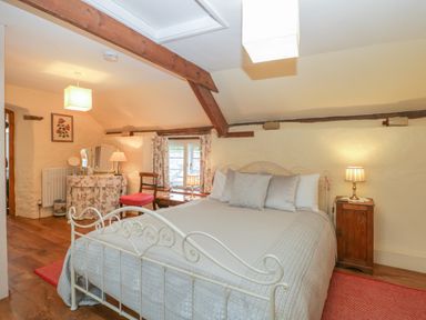 A bedroom with a double bed bedside table dressing table chair and wooden beams at The Old Bakery in Crowcombe