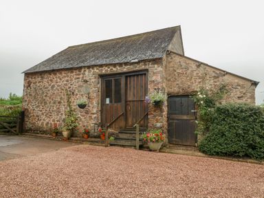 A stone barn with wooden double doors and surrounding plants at The Old Bakery in Crowcombe