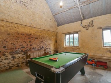 A room with a pool table a wooden bench and toy wagons by the windows at The Old Bakery in Crowcombe