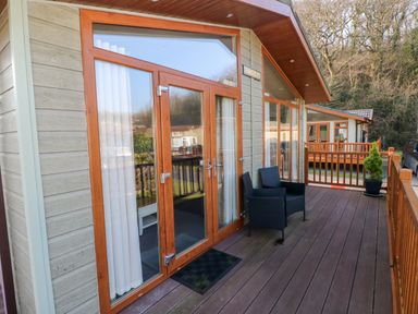 A wooden deck with black chairs potted plants and glass doors at Tranquillity - Heritage Park in Stepaside near Kilgetty