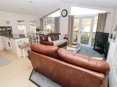 A living room with brown leather sofas a small coffee table and a dining area at Tranquillity - Heritage Park in Stepaside near Kilgetty