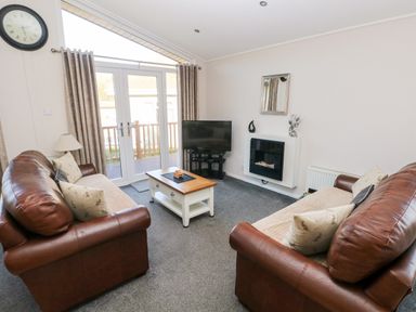 A living room with two brown leather sofas a coffee table a television and a wall-mounted fireplace at Tranquillity - Heritage Park in Stepaside near Kilgetty