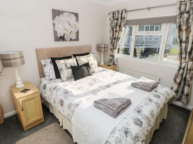 A bedroom with a double bed, bedside tables with lamps, pillows, and a window with curtains at Tranquillity - Heritage Park Stepaside near Kilgetty