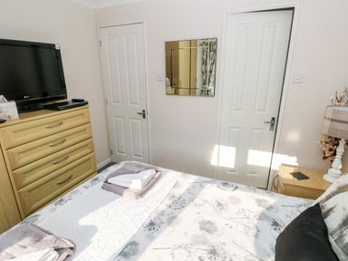 A bedroom with a bed with folded towels dresser with a television and two closed doors at Tranquillity - Heritage Park Stepaside near Kilgetty