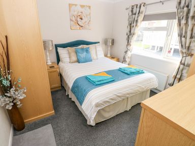 A bedroom with a double bed two bedside tables with lamps a wardrobe a chest of drawers and a window with curtains at Tranquillity - Heritage Park in Stepaside near Kilgetty
