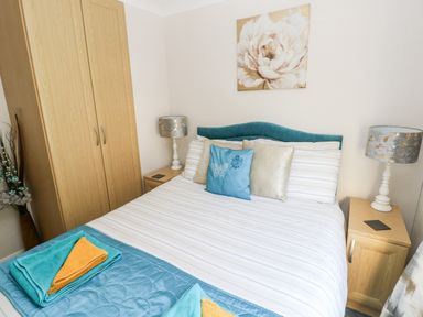 A bedroom with a double bed pillows bedside tables lamps and a wooden wardrobe at Tranquillity - Heritage Park in Stepaside near Kilgetty