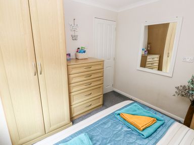 A bedroom with a wardrobe a chest of drawers a mirror and a bed with folded towels at Tranquillity - Heritage Park in Stepaside near Kilgetty