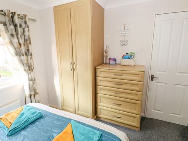 A bedroom with a bed, wardrobe, chest of drawers, and window with curtains at Tranquillity - Heritage Park Stepaside near Kilgetty