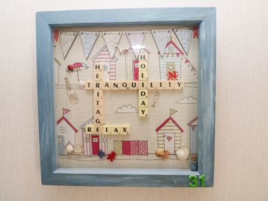 A decorative frame with scrabble tiles spelling holiday tranquility heritage relax on a background with beach huts at Tranquillity - Heritage Park in Stepaside near Kilgetty