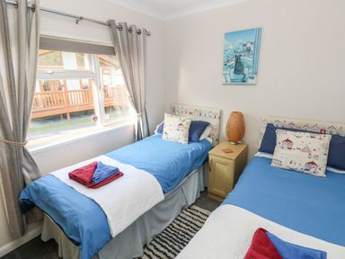 A bedroom with two single beds blue bedding and a nightstand with a lamp between them at Tranquillity - Heritage Park in Stepaside near Kilgetty