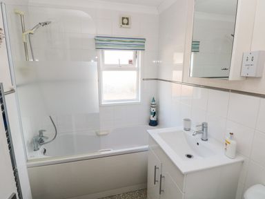 A bathroom with a bathtub shower combo a sink with a cabinet a window and a wall mirror at Tranquillity - Heritage Park in Stepaside near Kilgetty