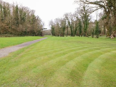 A grassy lawn with a gravel path and trees in the background at Tranquillity - Heritage Park in Stepaside near Kilgetty
