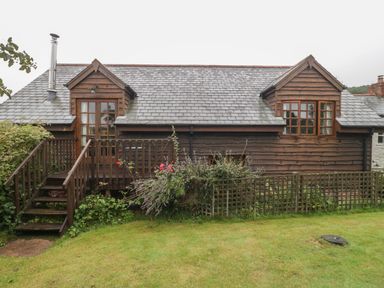 A wooden house with two dormer windows a small deck and steps leading to a garden at Floras Barn in Crowcombe