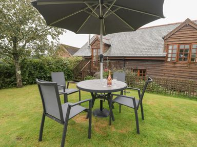 A garden with a round table and four chairs under an umbrella near a wooden house at Floras Barn in Crowcombe