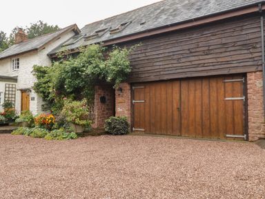 The exterior of a house with wooden garage doors climbing plants and gravel driveway at Floras Barn in Crowcombe