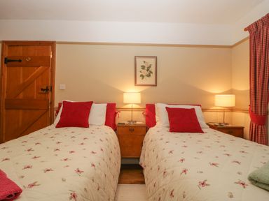 A bedroom with two beds with floral quilts and red pillows a wooden door and two bedside tables with lamps at Floras Barn in Crowcombe