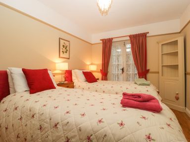 A bedroom with two single beds bedside tables lamps red cushions and red curtains at Floras Barn in Crowcombe