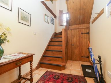 A hallway with wooden stairs a small wooden table with a vase and book a red patterned rug on tiled floor at Floras Barn in Crowcombe