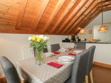 A dining table set for six with plates glasses and red napkins under a wooden sloped ceiling at Flora's Barn in Crowcombe