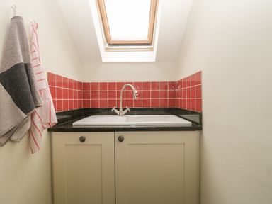 A small kitchen sink with red tiled backsplash under a skylight window at Floras Barn in Crowcombe